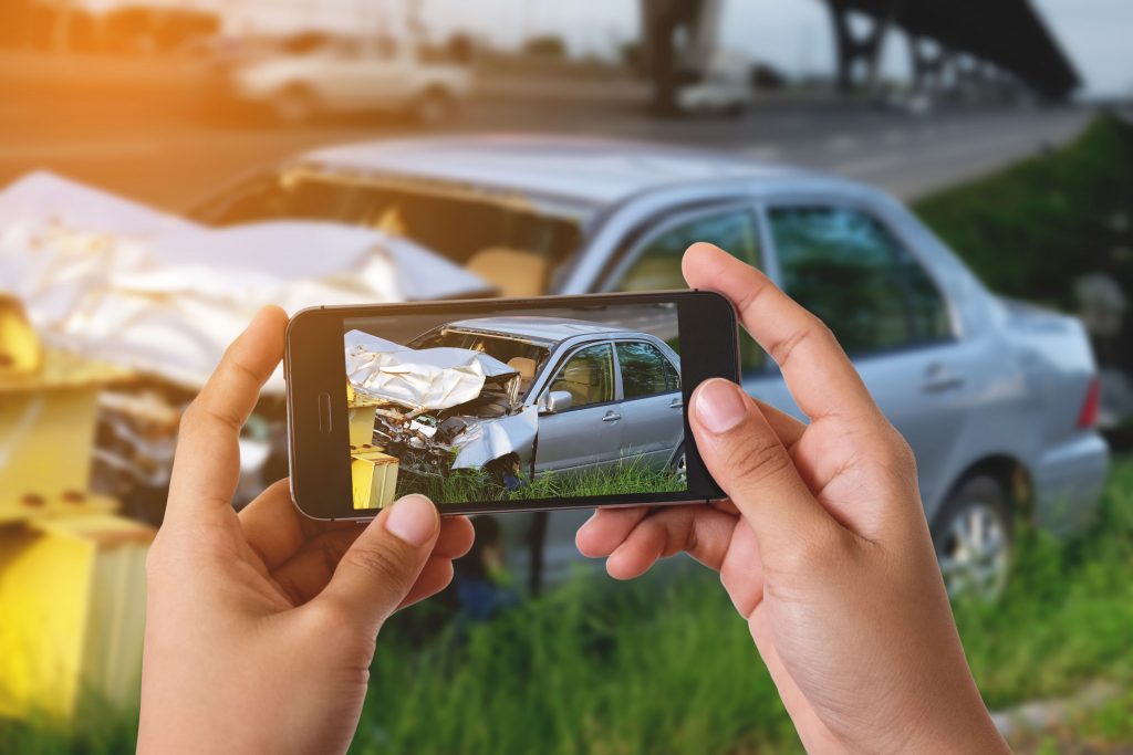 AdobeStock_126837010-compressor Hand holding a phone taking a picture of a damaged car