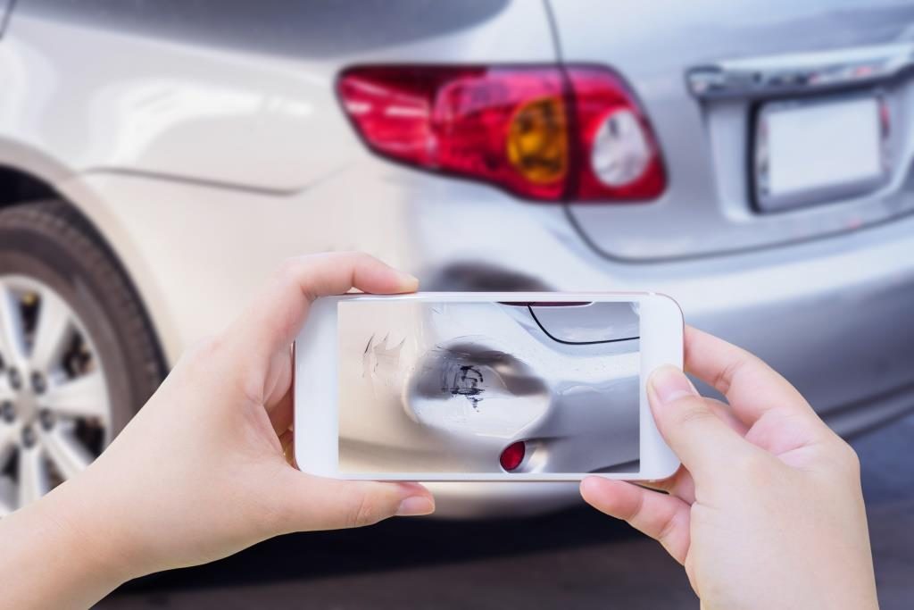 Hand holding a phone taking a picture of a damaged car